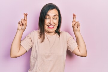 Wall Mural - Middle age hispanic woman wearing casual clothes gesturing finger crossed smiling with hope and eyes closed. luck and superstitious concept.