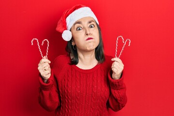 Sticker - Middle age hispanic woman wearing christmas hat holding candy puffing cheeks with funny face. mouth inflated with air, catching air.