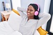 © Krakenimages.com - African american woman listening to music lying on bed at bedroom