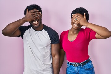 Sticker - Young african american couple standing over pink background smiling and laughing with hand on face covering eyes for surprise. blind concept.