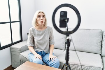 Poster - Young caucasian woman recording vlog tutorial with smartphone at home making fish face with lips, crazy and comical gesture. funny expression.