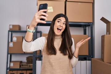 Canvas Print - Young brunette woman working at small business ecommerce taking selfie celebrating achievement with happy smile and winner expression with raised hand