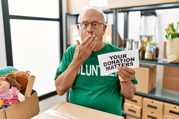 Wall Mural - Senior volunteer man holding your donation matters covering mouth with hand, shocked and afraid for mistake. surprised expression