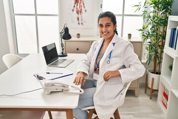 Canvas Print - Young hispanic woman wearing doctor uniform looking to the camera at clinic