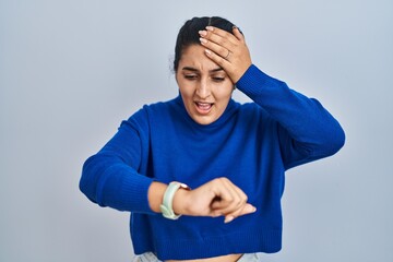 Wall Mural - Young hispanic woman standing over isolated background looking at the watch time worried, afraid of getting late