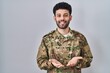 © Krakenimages.com - Arab man wearing camouflage army uniform smiling with hands palms together receiving or giving gesture. hold and protection