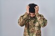 Arab man wearing camouflage army uniform suffering from headache desperate and stressed because pain and migraine. hands on head.