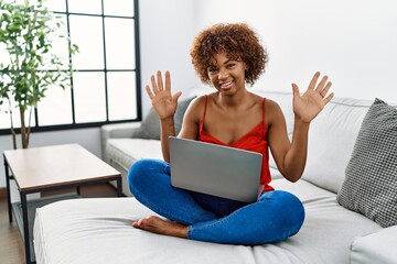 Canvas Print - Young african american woman sitting on the sofa at home using laptop showing and pointing up with fingers number ten while smiling confident and happy.