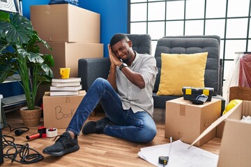 Wall Mural - African american man sitting on the floor at new home sleeping tired dreaming and posing with hands together while smiling with closed eyes.