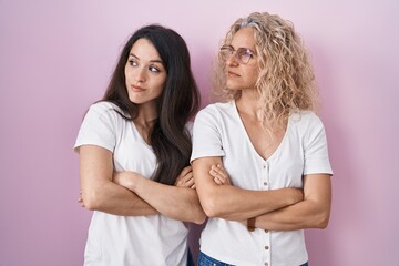 Sticker - Mother and daughter standing together over pink background looking to the side with arms crossed convinced and confident