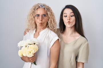 Sticker - Mother and daughter holding bouquet of white flowers making fish face with lips, crazy and comical gesture. funny expression.