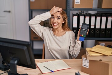 Wall Mural - Hispanic woman working at small business ecommerce holding credit card and dataphone stressed and frustrated with hand on head, surprised and angry face