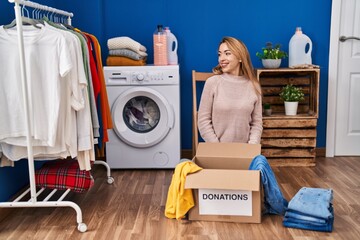 Poster - Hispanic woman putting clothes in donation box looking away to side with smile on face, natural expression. laughing confident.