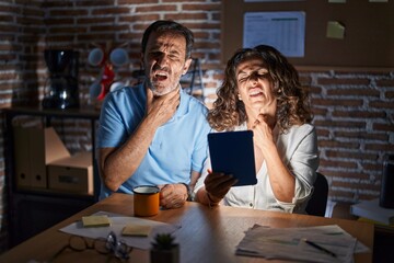 Sticker - Middle age hispanic couple using touchpad sitting on the table at night touching painful neck, sore throat for flu, clod and infection