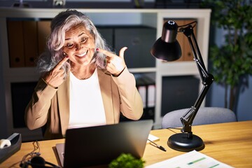 Sticker - Middle age woman with grey hair working using computer laptop late at night smiling cheerful showing and pointing with fingers teeth and mouth. dental health concept.