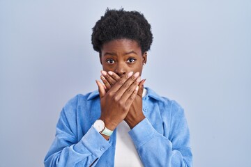 Wall Mural - African american woman standing over blue background shocked covering mouth with hands for mistake. secret concept.