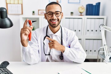 Canvas Print - African american doctor man holding ear otoscope at the clinic smiling happy pointing with hand and finger