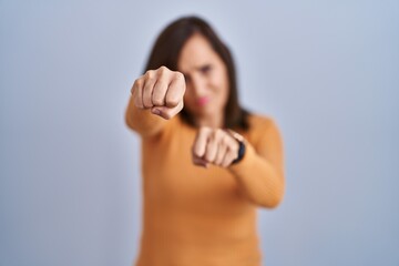 Sticker - Middle age brunette woman standing wearing orange sweater punching fist to fight, aggressive and angry attack, threat and violence