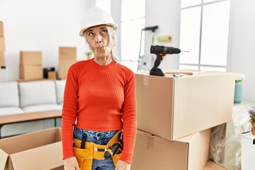 Sticker - Middle age grey-haired woman wearing hardhat standing at new home making fish face with lips, crazy and comical gesture. funny expression.