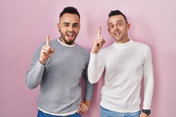 Wall Mural - Homosexual couple standing over pink background pointing finger up with successful idea. exited and happy. number one.