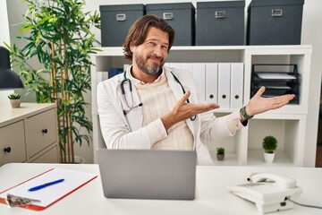 Canvas Print - Handsome middle age doctor man working at the clinic inviting to enter smiling natural with open hand