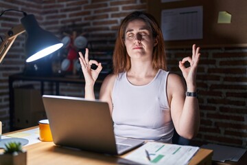 Poster - Brunette woman working at the office at night relax and smiling with eyes closed doing meditation gesture with fingers. yoga concept.