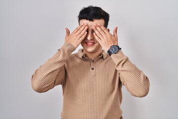 Poster - Non binary person standing over isolated background covering eyes with hands smiling cheerful and funny. blind concept.