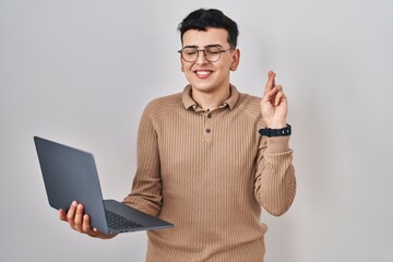 Wall Mural - Non binary person using computer laptop gesturing finger crossed smiling with hope and eyes closed. luck and superstitious concept.