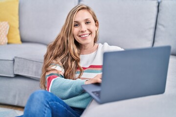 Wall Mural - Young blonde woman using laptop sitting on floor at home