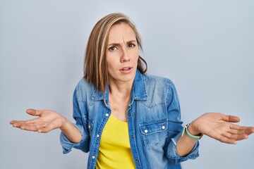 Canvas Print - Young blonde woman standing over blue background clueless and confused with open arms, no idea concept.