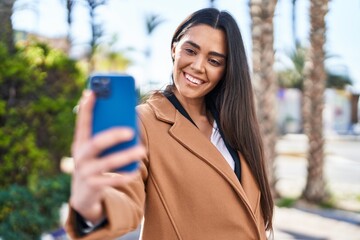 Wall Mural - Young hispanic woman smiling confident making selfie by the smartphone at park