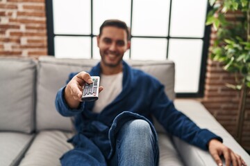 Wall Mural - Young hispanic man watching tv sitting on sofa at home