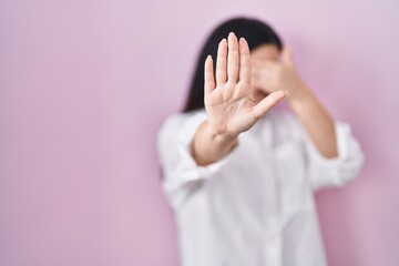 Canvas Print - Young brunette woman standing over pink background covering eyes with hands and doing stop gesture with sad and fear expression. embarrassed and negative concept.