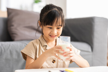 Happy Asian Kid drinking fresh milk for good health at home.Enjoy and tasty for strong bone.Female kid drink soy milk from glass tasty and delicious with calcium.Healthy Lifestyle Concept