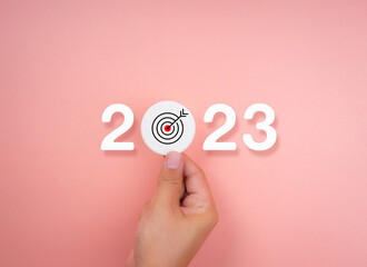 Poster - 2023 Happy New year background banner. Two thousand Twenty-Three year numbers on pink background with hand holding target icon. Welcome, Merry Christmas, and business goals in 2023 year calendar.