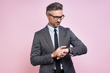 Confident Mature Man In Formalwear Checking The Time While Standing Against Pink Background