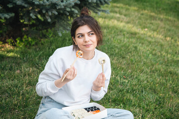 A young woman eating sushi in the park, picnic in nature.