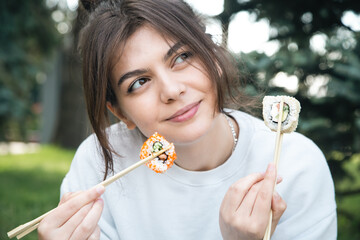 Wall Mural - A young woman eating sushi in the park, picnic in nature.