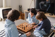 © Anna - Brothers playing the checkers at home, siblings playing the board strategy game, spending time together.