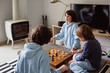 © Anna - Brothers playing the checkers at home, siblings playing the board strategy game, spending time together.