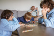 © Anna - Three brothers playing board game Mikado at home while the father checking his smartphone, family fun, siblings spending time together.