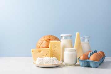 Variety of dairy products on blue background. Jug of milk, cheese, butter, yogurt or sour cream, cottage cheese, bread and eggs. Farm dairy products concept