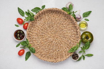 Wall Mural - Italian food on white background around wicker round tray. Fresh green and red basil, tomatoes, parmesan cheese, olives, olive oil, spices, spaghetti pasta. Mediterranean Kitchen