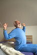 © Solid photos - Senior man stretching while sitting in bed after waking up in the morning