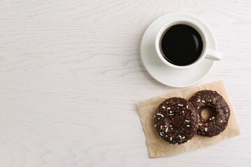 Two delicious fresh donuts with sprinkles and cup of coffee on white wooden table, flat lay. Space for text