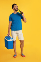 Wall Mural - Happy man with cool box drinking beer on yellow background