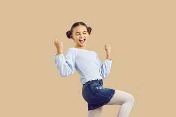 Happy kid celebrating success. Adorable child celebrating victory. Pretty little girl with cute hair buns feeling triumphant, excited and overjoyed, shouting Yes, I did it and raising fists up