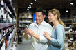 Young diverse couple man and woman in liquor department choosing wine, smiling and happy using smartphone to identify wine, using app to scan products