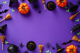 Fototapeta Kawa jest smaczna - Happy Halloween holiday banner design. Frame made of Halloween decorations, orange pumpkins, witch's pots and brooms, spiders, bats on purple background. Flat lay, top view, copy space.