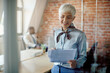 © Drazen - Happy senior businesswoman analyzing paperwork while working at corporate office.